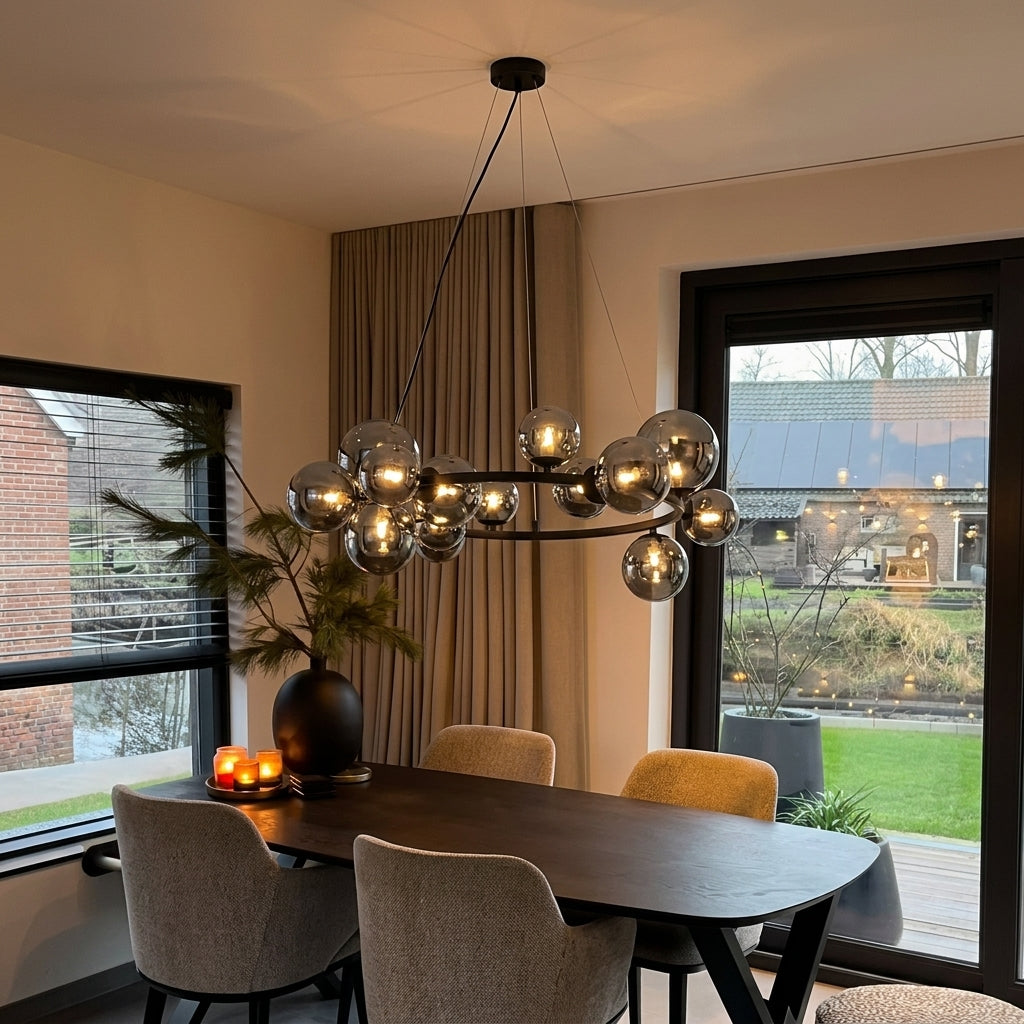 A modern multi-light chandelier with spherical glass globes hanging over a dark wood dining table in a contemporary dining room with beige chairs and large windows.
