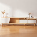 A modern light wood media console with white cabinet doors and tapered legs, styled in a minimalist room with a light wood floor and white wall.