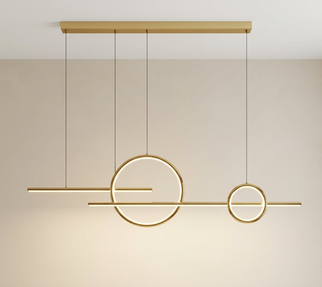 Modern linear pendant light fixture with gold-toned metal bars and glowing circular ring elements, suspended from a rectangular ceiling canopy against a warm beige wall.