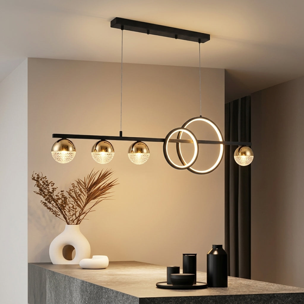 Modern multi-light pendant chandelier with a black metal frame, three spherical glass shades, two circular ring lights, and two smaller globe shades, shown hanging in a contemporary interior above a stone counter.