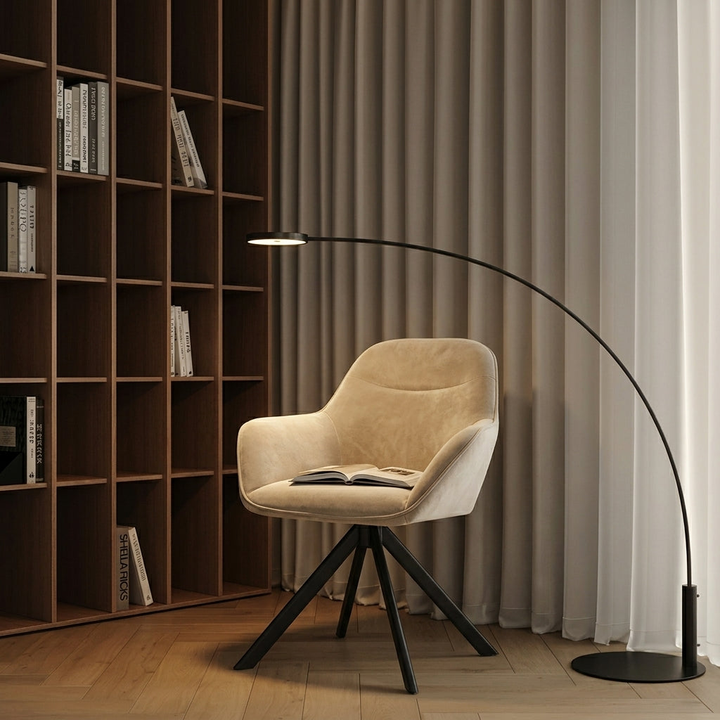 A modern black arched floor lamp stands beside a beige upholstered swivel chair in a styled interior with a wooden bookshelf and curtains.