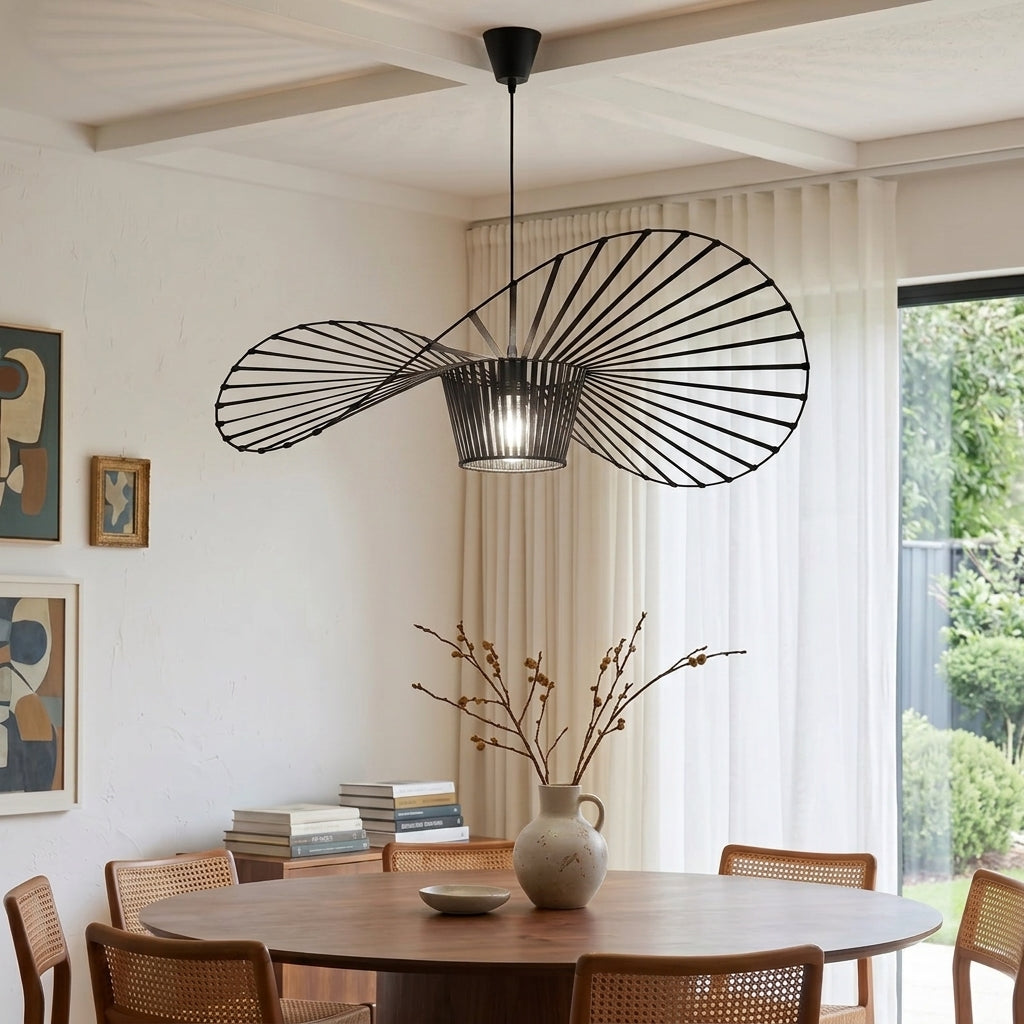 A modern black metal pendant light with a fan-like radial wire design hangs over a round wooden dining table in a bright, neutral-toned dining room.