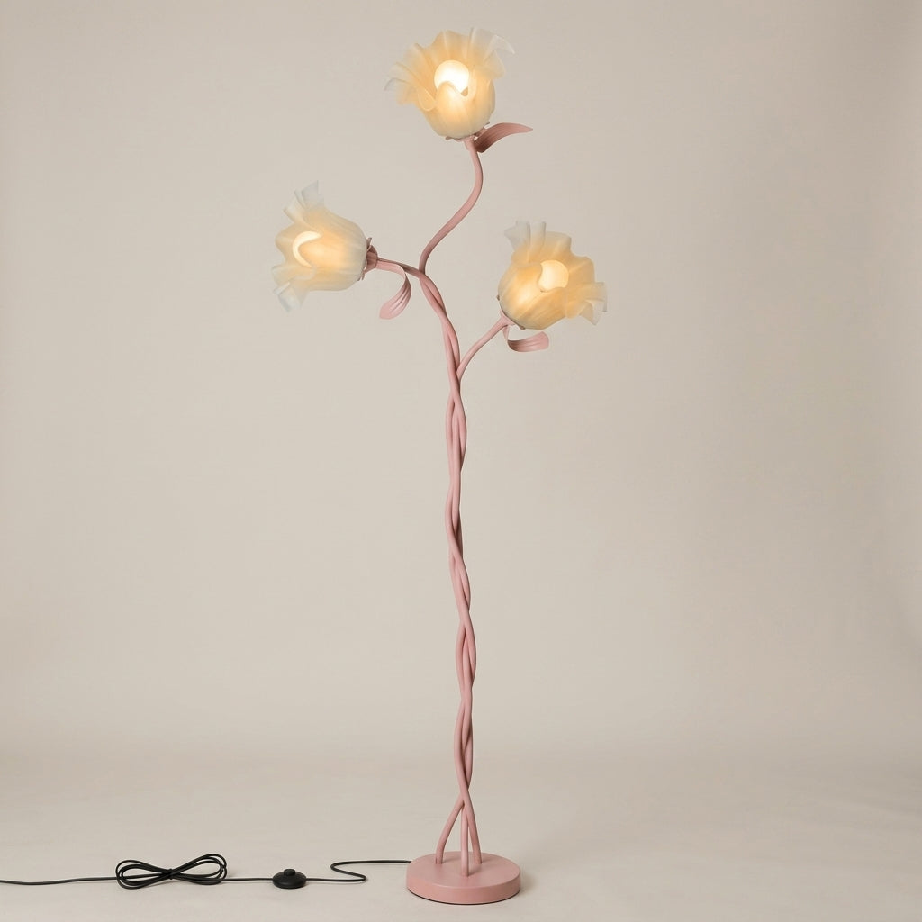 A whimsical floor lamp designed like a flowering vine, featuring a twisted pink metal stem and three glowing flower-shaped shades, set against a plain light beige background.