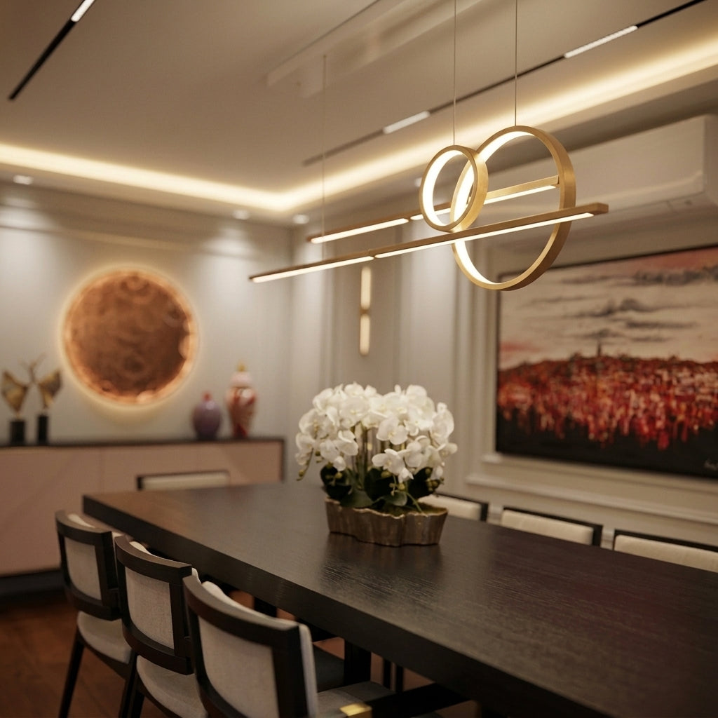Modern dining room interior with a long dark wood table, upholstered dining chairs, a gold geometric pendant light, white orchids on the table, and wall art in the background.