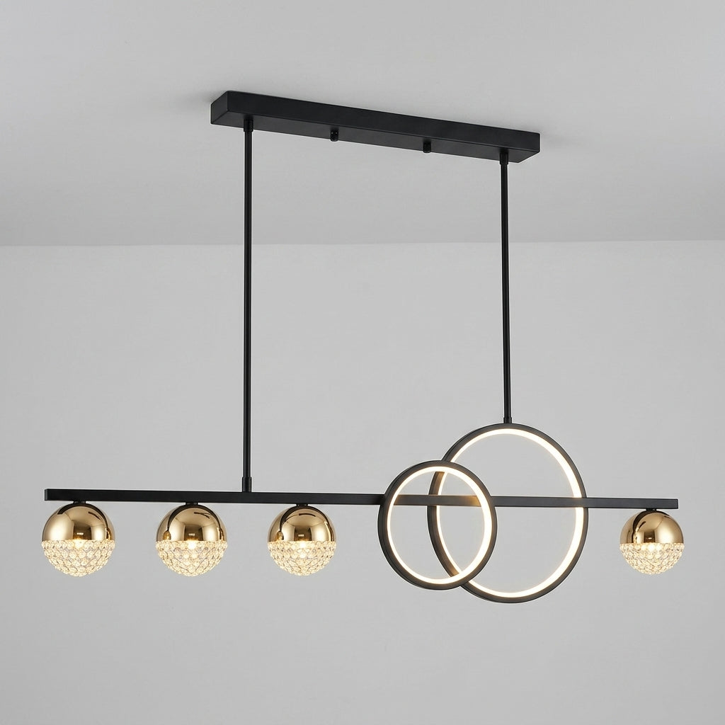 Modern linear chandelier with five gold spherical shades and two interlocking circular ring elements, suspended from a black ceiling mount against a light gray wall.