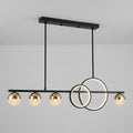 Modern linear chandelier with five gold spherical shades and two interlocking circular ring elements, suspended from a black ceiling mount against a light gray wall.
