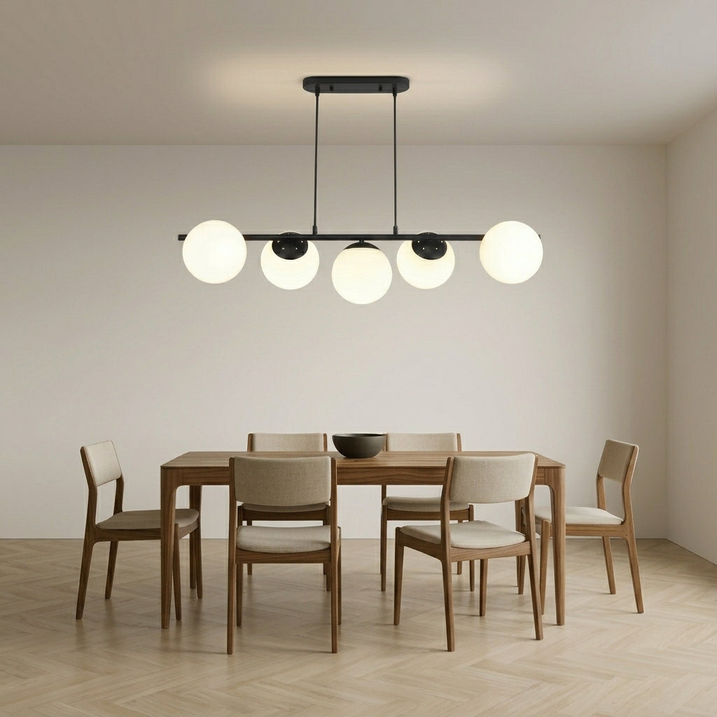 Modern linear chandelier with five spherical white glass shades and black hardware, hanging above a wooden dining table and six upholstered chairs in a minimalist dining room.