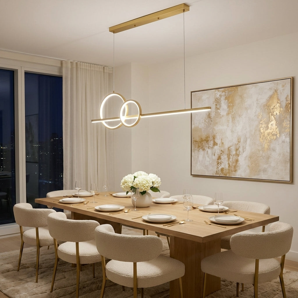 Modern linear pendant light with two interlocking circular rings, suspended over a wooden dining table with upholstered chairs in a contemporary dining room.