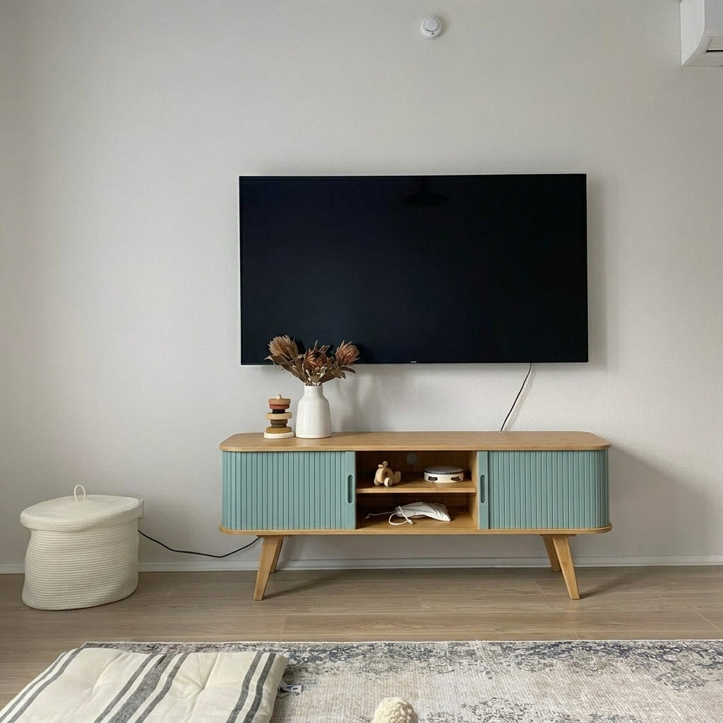 A mid-century modern TV stand with ribbed sage green doors and light wood legs, styled in a minimalist living room under a wall-mounted flat-screen TV.
