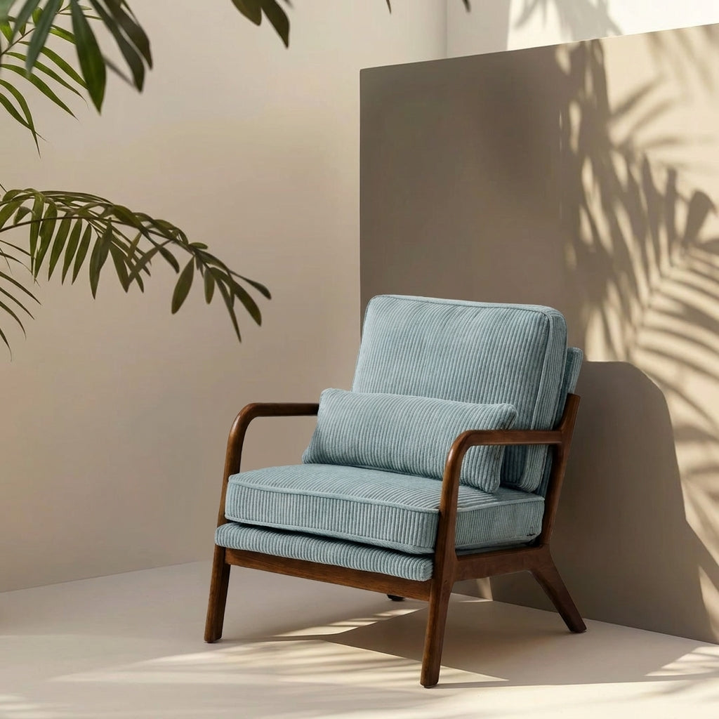 A modern armchair with light blue ribbed fabric cushions and a dark wood frame, styled in a minimalist room with palm leaf shadows on a beige wall.