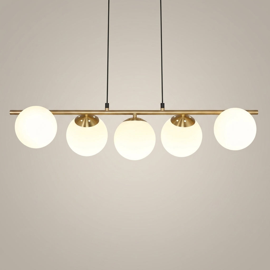 A modern linear pendant light fixture with five spherical frosted glass shades and a brushed brass metal bar, suspended by black cords against a neutral light gray background.