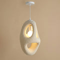 An organic-shaped pendant light with a textured, organic beige concrete-like body, suspended from a white ceiling canopy against a warm beige wall.