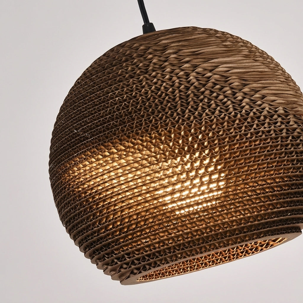 A spherical woven pendant light shade made from natural brown wicker or rattan, glowing warm yellow from an integrated light, suspended against a plain light gray background.