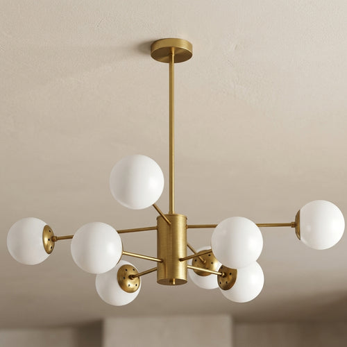 A modern six-light sputter-style ceiling light fixture with a brushed brass/gold metal frame and white spherical glass shades, shown hanging from a ceiling in an indoor room setting.