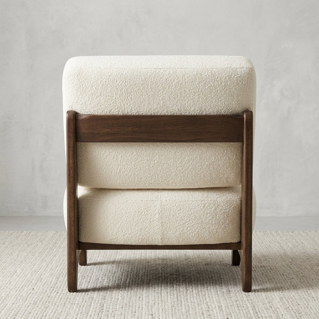 A modern upholstered accent chair with cream bouclé fabric and a dark brown wooden frame, shown from the back against a textured light gray wall and neutral rug.