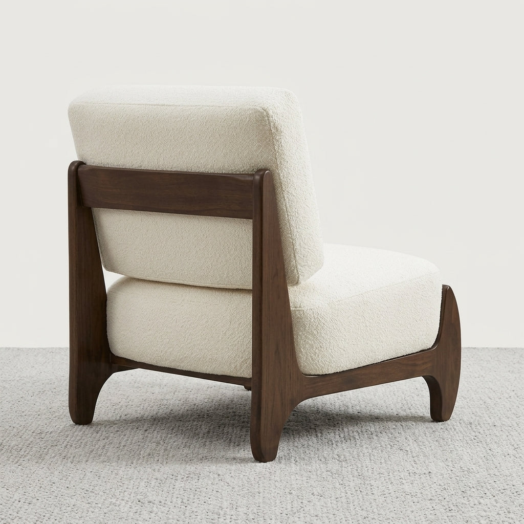 A modern accent chair with cream bouclé upholstery and a dark brown wooden frame, shown from a three-quarters angle on a textured gray carpet against a light off-white wall.