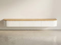 A minimalist wall-mounted floating cabinet with a light natural wood top and white curved lower body, shown against a plain off-white wall and concrete floor.